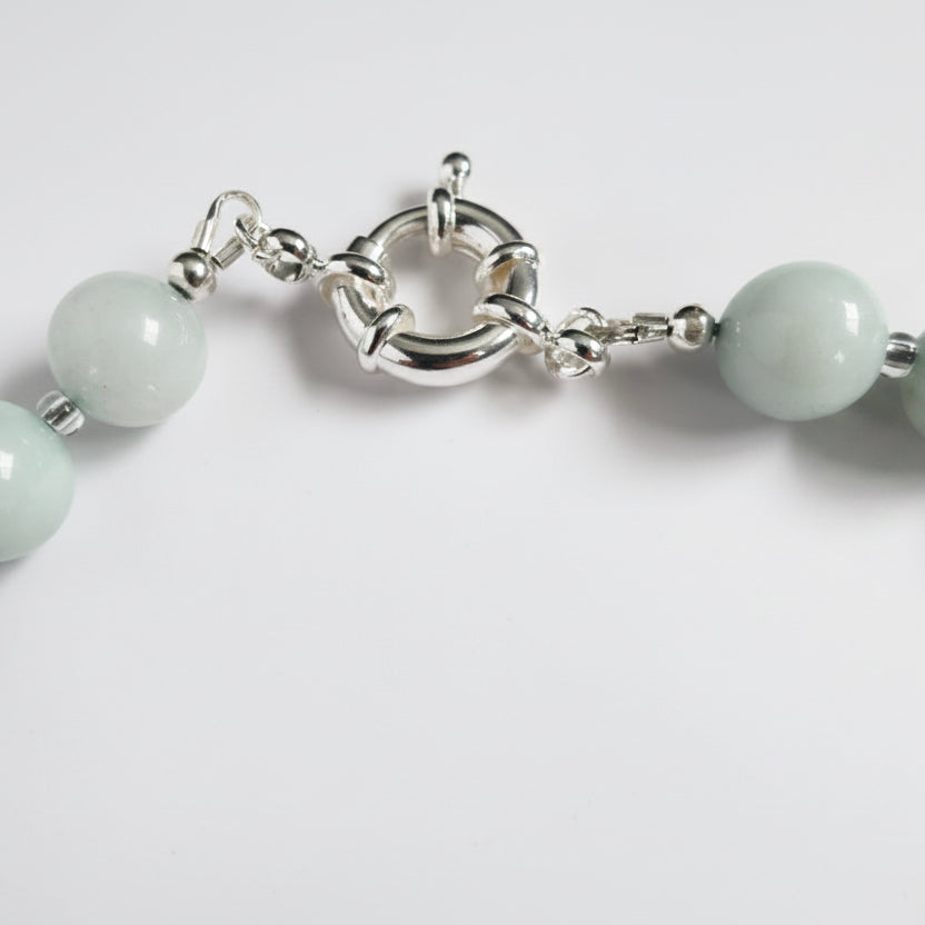 Close-up of a bracelet with light green beads and a silver clasp on a white background